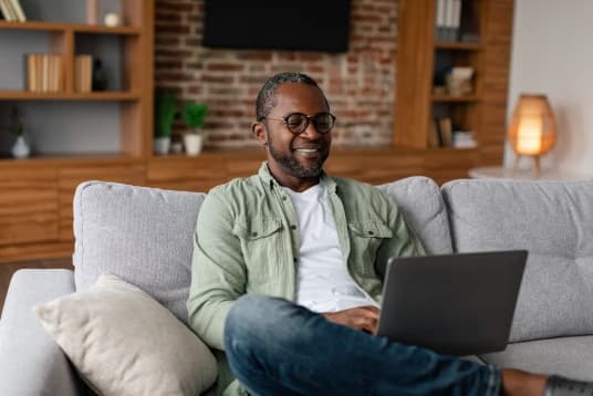 Homem fazendo terapia pelo Total Mind. A imagem tem um homem mais velho, mexendo no notebook e sentado no sofá da sala.